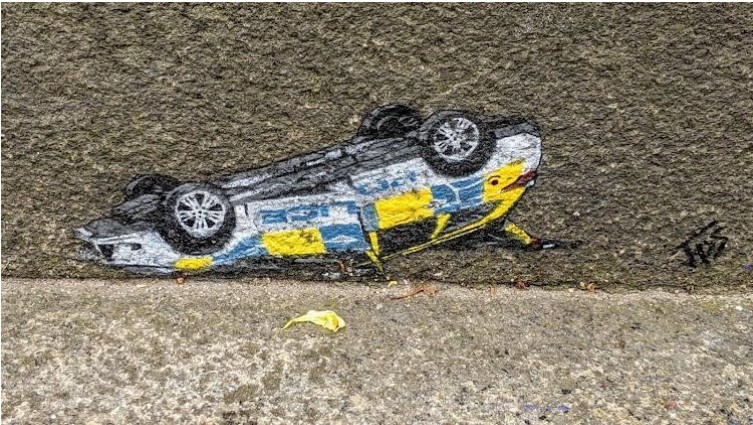 Das Grafitto eines umgedrehten Polizeiautos des Straßenkünstlers JPS aus England. 